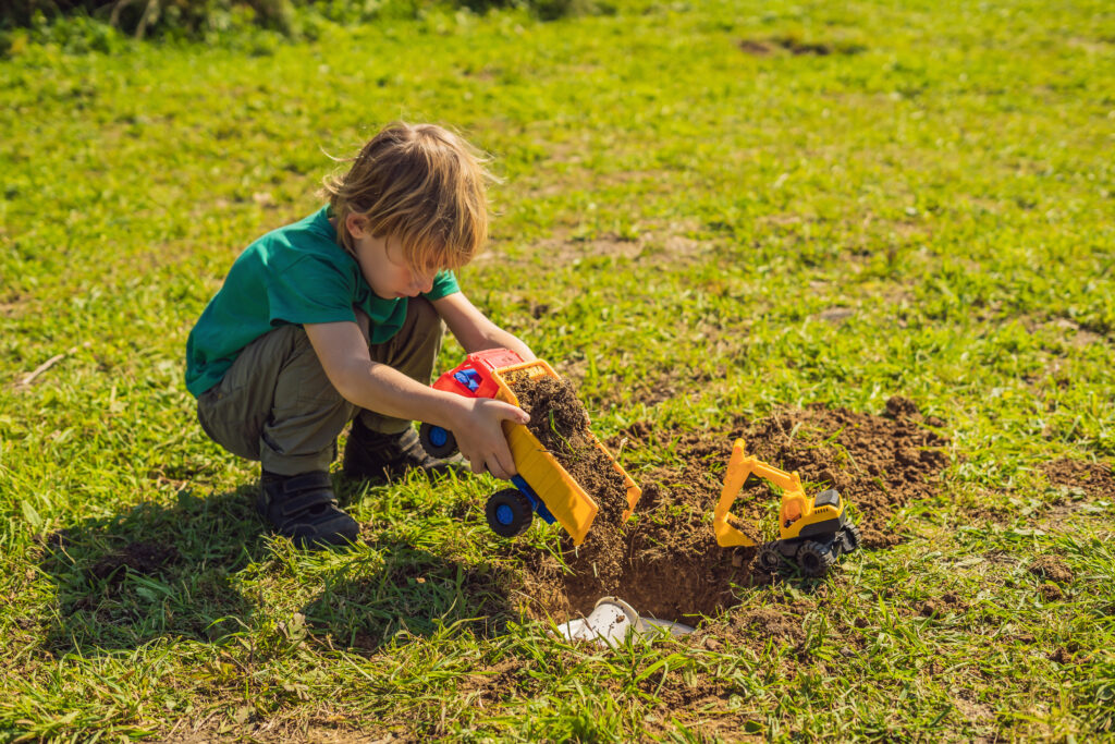 An image of a young boy with a digger truck toy, digging up grass.