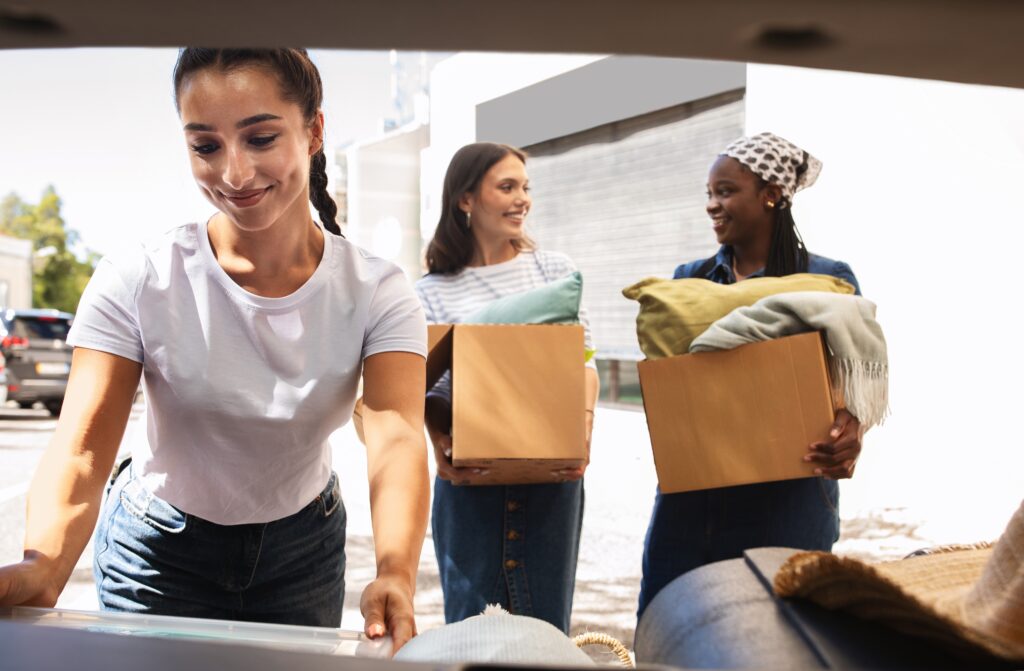 Three female students packing boxes into the boot of a car.