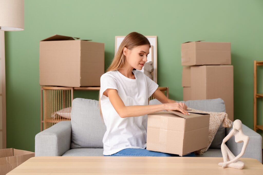 A woman sat on a sofa and unpacking moving boxes.