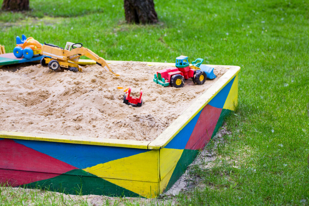 An image of a sandpit in a garden with toys inside.